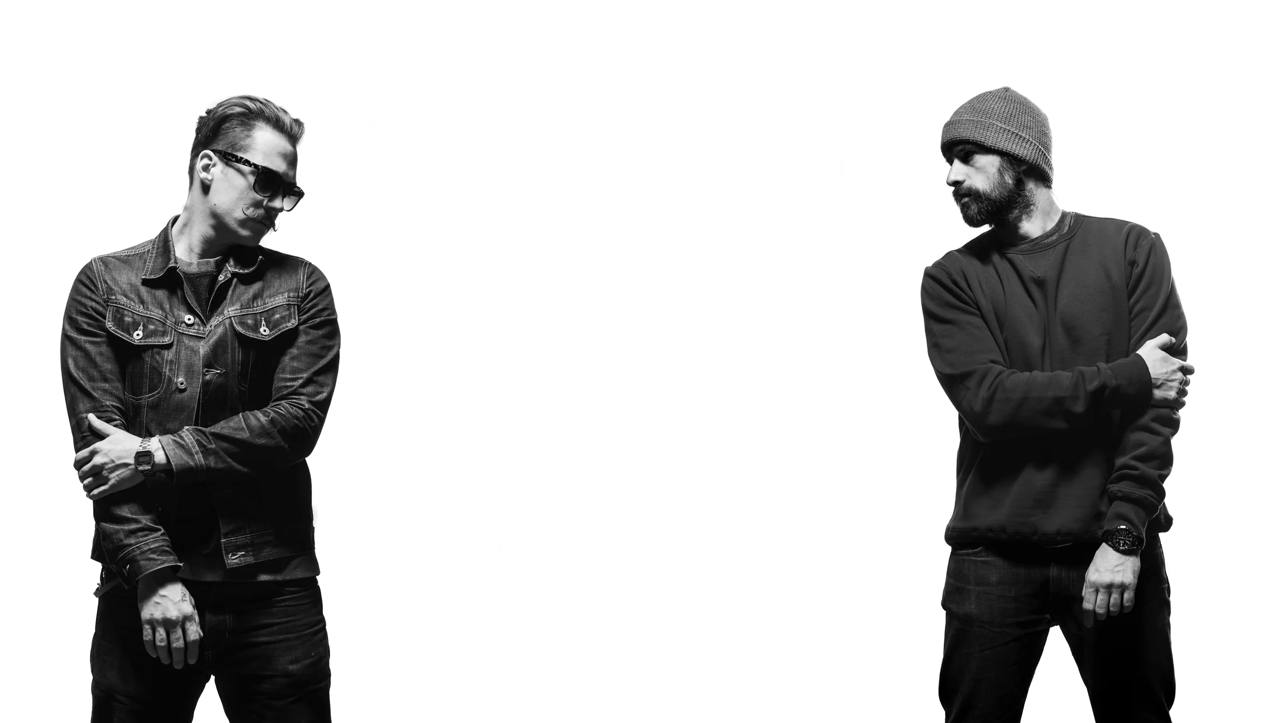 Two of the Kiddo Motors crew, in black and white, standing at either edge of a white studio wall and glancing at each other